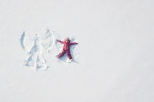 Child girl playing and making a snow angel in the snow. Top flat overhead view